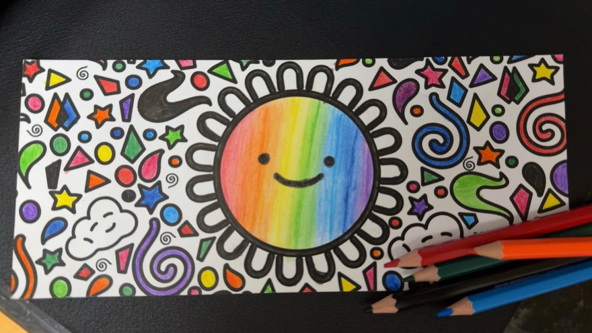 A care kit card coloured in with a rainbow sun, surrounded by doodled shapes, with coloured pencils beside it