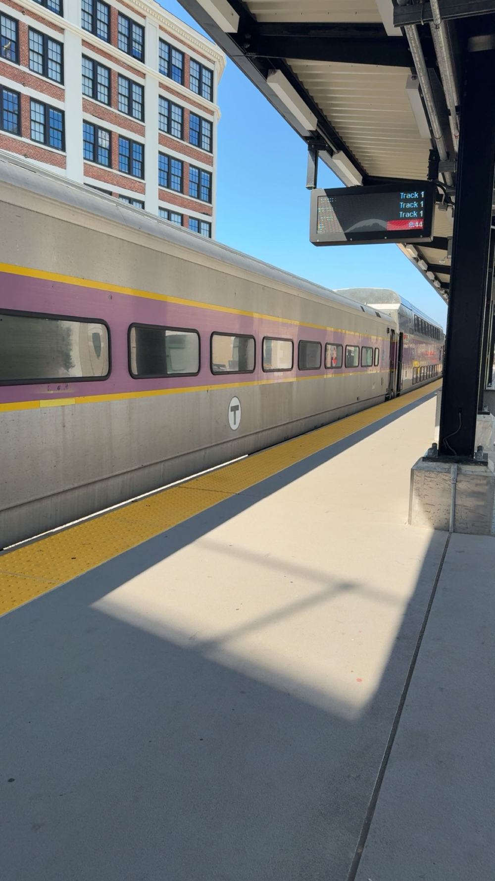 An MBTA commuter rail train waiting at the platform in morning sun